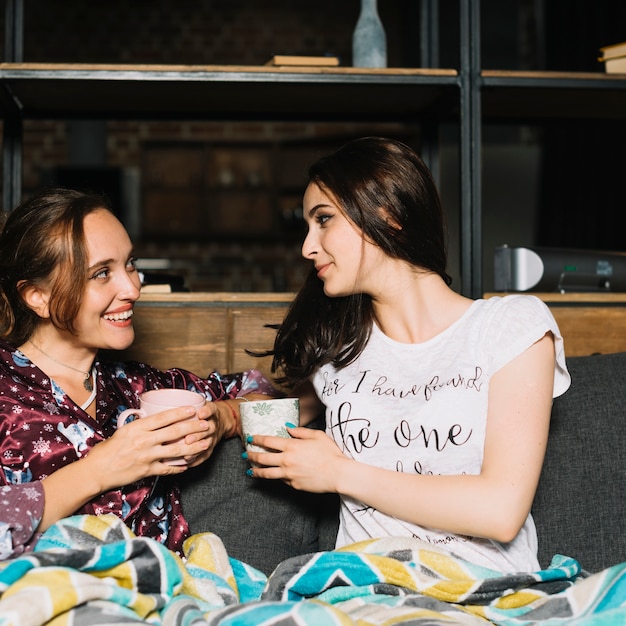 Two young women with cup of coffee looking at each other