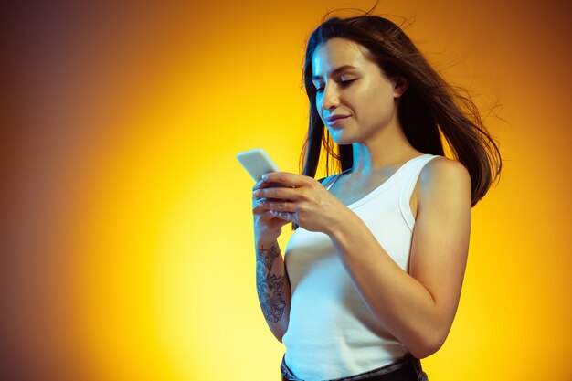 Typing. Portrait of young caucasian woman isolated on gradient yellow studio wall