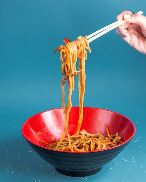 Free photo udon stir fried noodles with bell pepper carrot spring onion soy sauce and sesame in a bowl