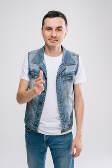 Ufa, russia - 31 march 2020. handsome young caucasian man in denim clothes pointing his finger at you. concept of wagering bright emotions by a professional actor.