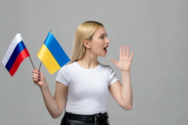 Ukraine russian conflict blonde cute girl holding russian and ukrainian flag yelling at someone