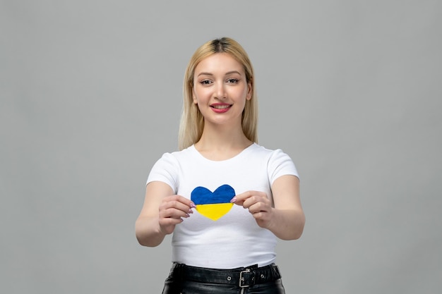 Free photo ukraine russian conflict blonde cute girl holding ukrainian heart smiling