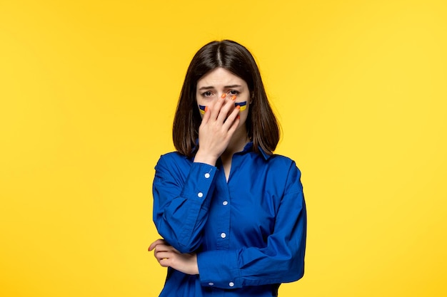 Ukraine russian conflict cute young girl in blue shirt yellow background crying covering face