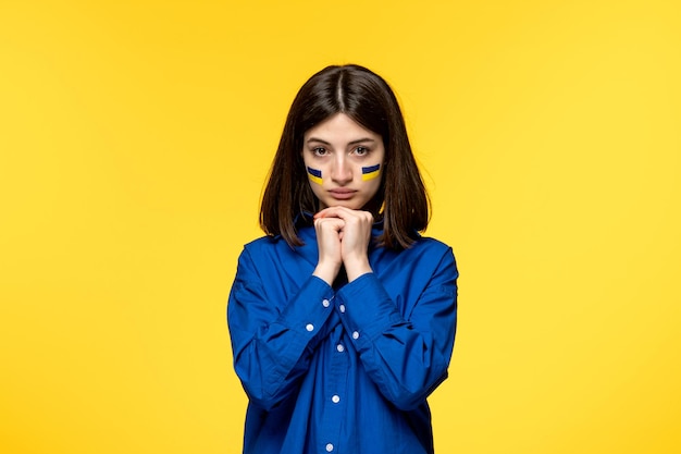 Ukraine russian conflict cute young girl in blue shirt yellow background praying