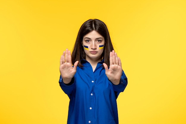 Ukraine russian conflict cute young girl in blue shirt yellow background raising both hands stop