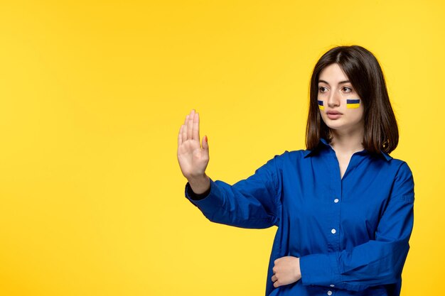 戦争に停止すると言っている青いシャツの黄色の背景でウクライナロシア紛争かわいい若い女の子