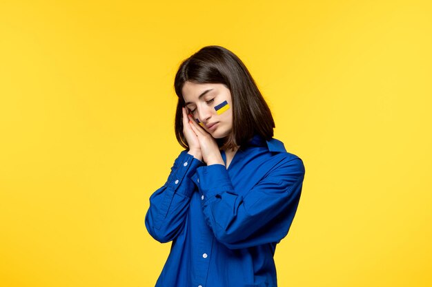 Ukraine russian conflict cute young girl in blue shirt yellow background tired want to sleep