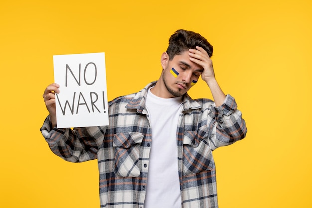 Free photo ukraine russian conflict cute young handsome guy with flags on cheeks scared with no war sign