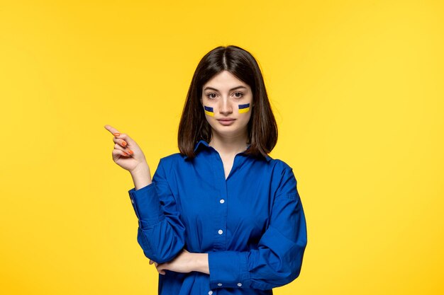 Ukraine russian conflict dark hair cute girl with flags on cheeks pointing left being serious