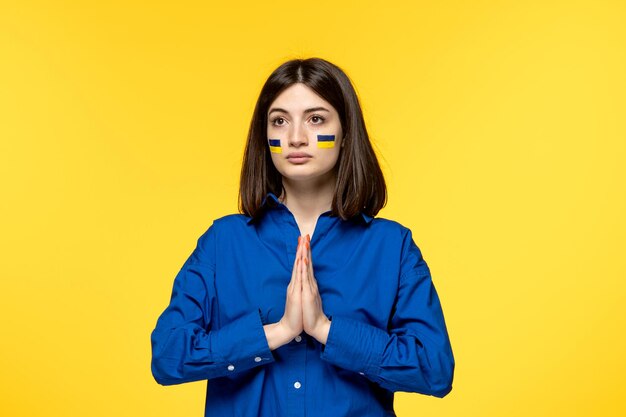 Ukraine russian conflict dark hair cute girl with flags on cheeks praying looking up