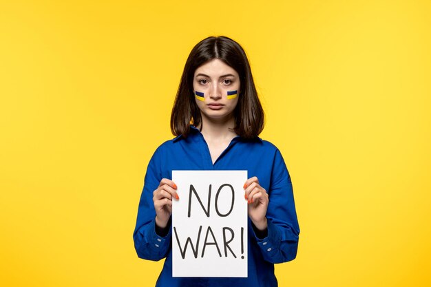 Ukraine russian conflict dark hair cute girl with flags on cheeks with no war sign on paper