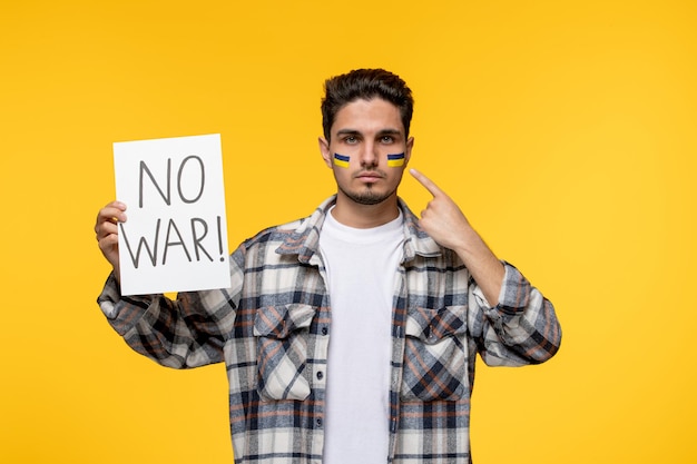 Free photo ukraine russian conflict handsome courageous guy with flags on cheeks standing with no war sign