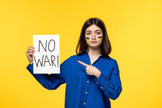 Free photo ukraine russian conflict pretty cute girl with flags on cheeks holding no war sign