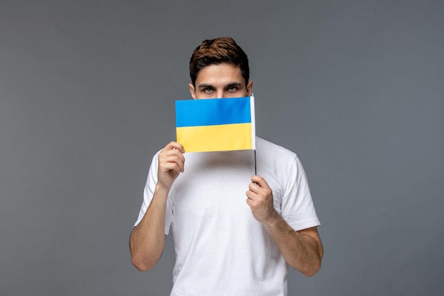 Free photo ukraine russian conflict pretty cute handsome man in white shirt with covering face with flag