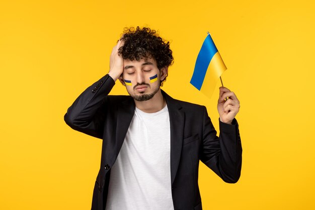 Ukraine russian conflict young guy in blazer painted ukrainian flag on face holding head