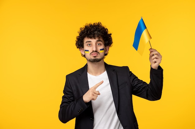 Ukraine russian conflict young guy in blazer painted ukrainian flag on face pointing at flag