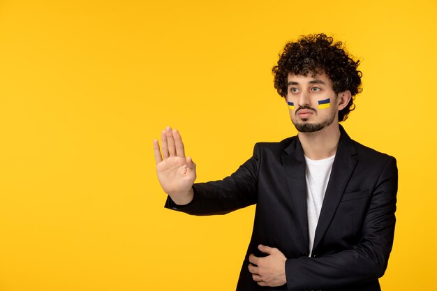 Ukraine russian conflict young guy in blazer painted ukrainian flag on face stop hand gesture