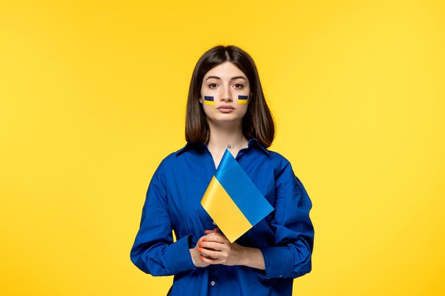Ukraine russian conflict young pretty girl flags on cheeks yellow background being silent