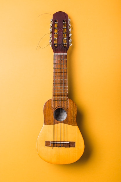 Ukulele with broken string on yellow background