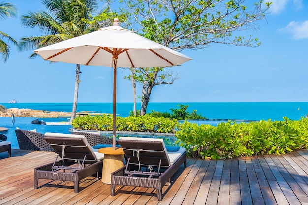 Umbrella and chair around outdoor swimming pool in hotel resort with sea ocean view for travel vacation