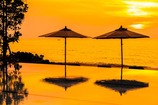 Зонтик и стул вокруг бассейна рядом с морем и океаном на рассвете или закате