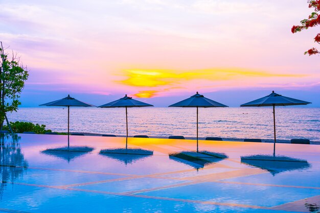 Umbrella and chair around swimming pool neary sea ocean beach at sunrise or sunset time