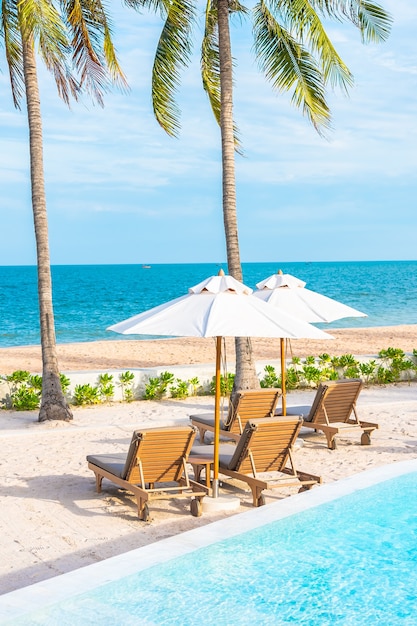 Umbrella and deck chair around outdoor swimming pool in hotel resort with sea ocean beach and coconut palm tree