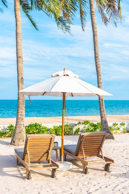 Umbrella and deck chair around outdoor swimming pool in hotel resort with sea ocean beach and coconut palm tree