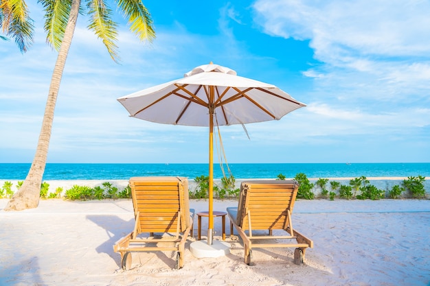 Зонтик и шезлонг вокруг открытого бассейна в курортном отеле с пляжем на берегу океана и кокосовой пальмой