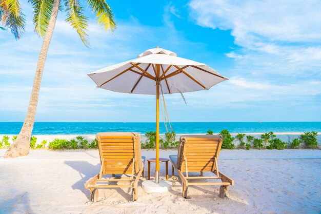 Зонтик и шезлонг вокруг открытого бассейна в курортном отеле с пляжем на берегу океана и кокосовой пальмой