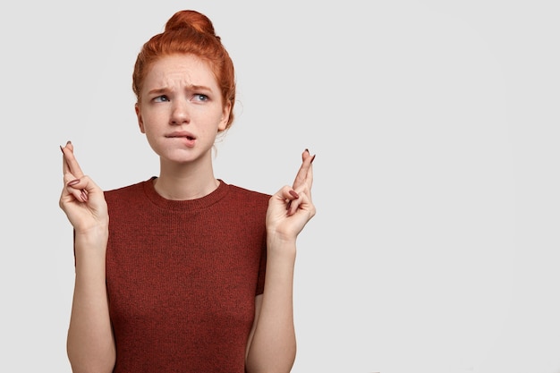 Unaware ginger girlfriend looks superstitious, crosses fingers for having success or good luck, bites lips