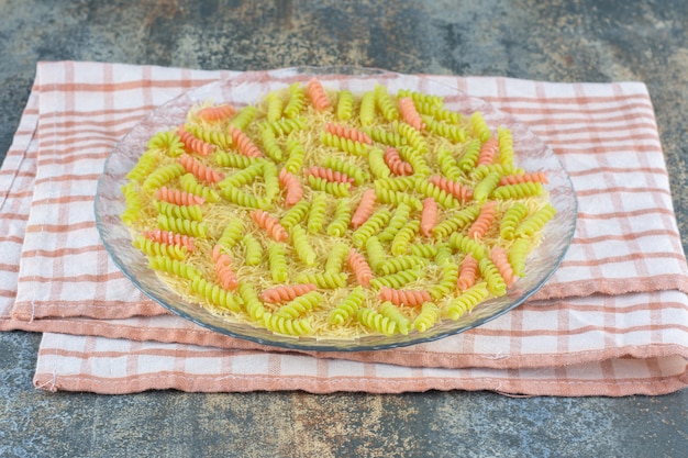 Unbaked fusilli pasta in the glass bowl, on towel , on the marble surface.