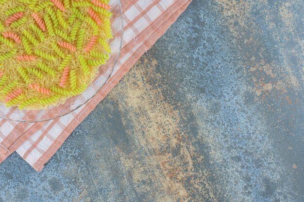 Unbaked fusilli pasta in the glass bowl, on towel , on the marble surface.