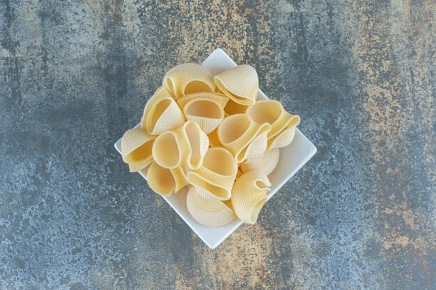 Невыпеченные макароны в миске на мраморной поверхности.
