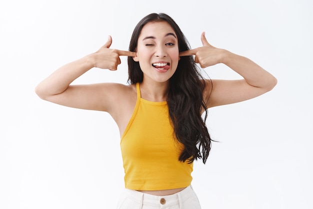 Unbothered, carefree pretty east-asian girl uninterested what are you talking about, acting silly, put fingers in ears and showing tongue, making goofy grimace, being childish, white background