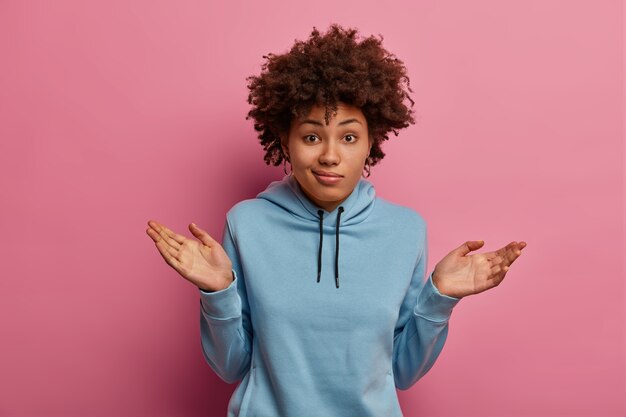 Uncertain doubtful Afro American woman spreads palms, shrugs shoulders, has no idea