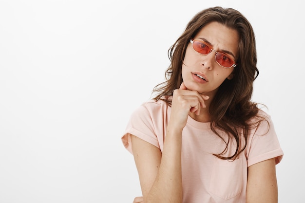 Uncertain girl with sunglasses posing against the white wall