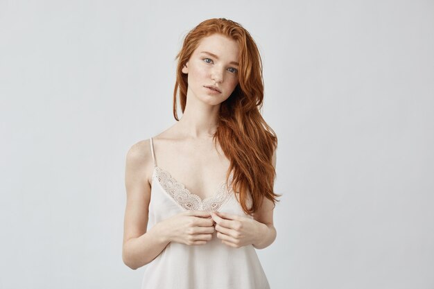 Uncertain young ginger and freckled in bodoir lingerie in the morning on white wall.