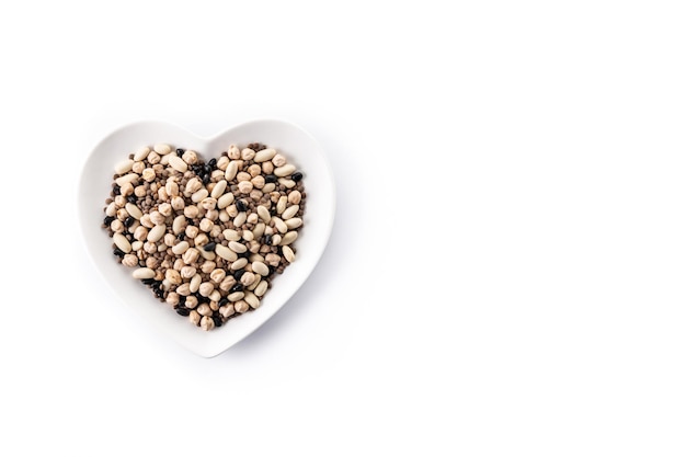 Uncooked assorted legumes in heart shape plate isolated on white background