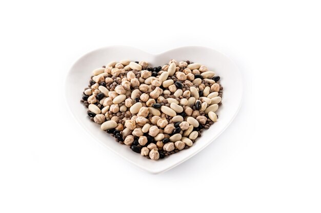 Uncooked assorted legumes in heart shape plate isolated on white background