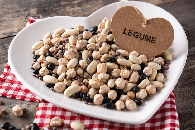 Uncooked assorted legumes in heart shape plate on rustic wooden table