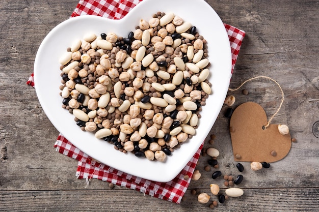 Free photo uncooked assorted legumes in heart shape plate on rustic wooden table.