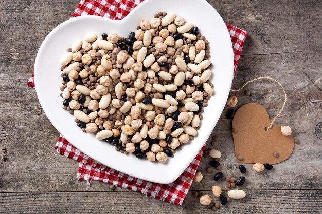 Uncooked assorted legumes in heart shape plate on rustic wooden table.