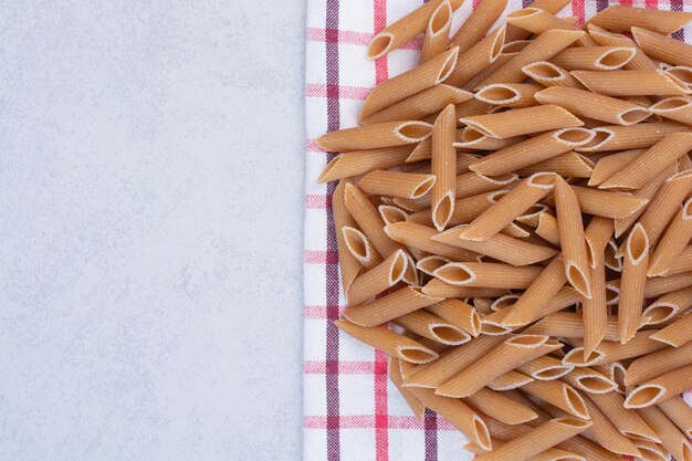 Uncooked brown penne pasta on striped tablecloth