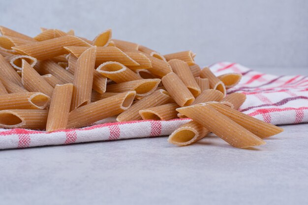 Uncooked brown penne pasta on striped tablecloth