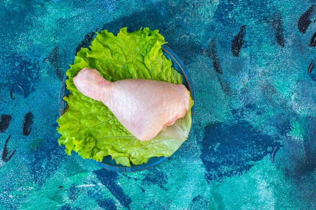 Free photo uncooked chicken drumstick on a lettuce in a plate