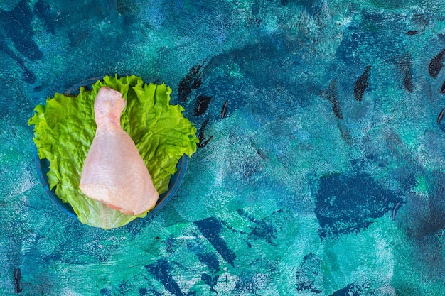 Uncooked chicken drumstick on a lettuce in a plate