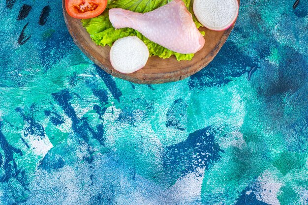 Uncooked chicken drumstick next to tomatoes ,radish on a board