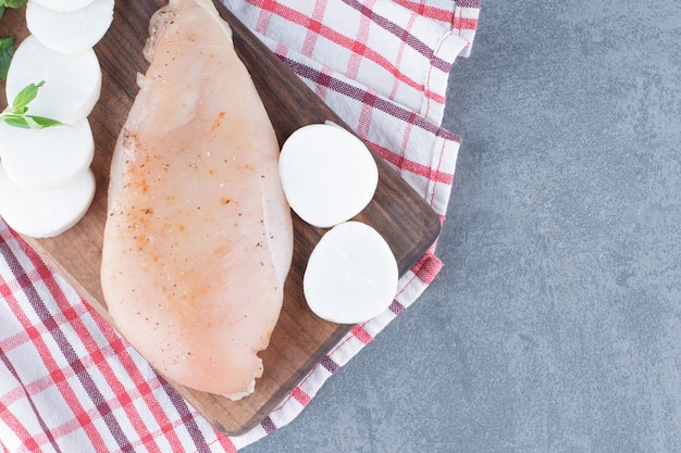 Uncooked chicken fillet with radish slices on wooden board.