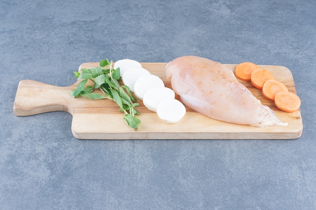 Uncooked chicken fillet with vegetables on wooden board.